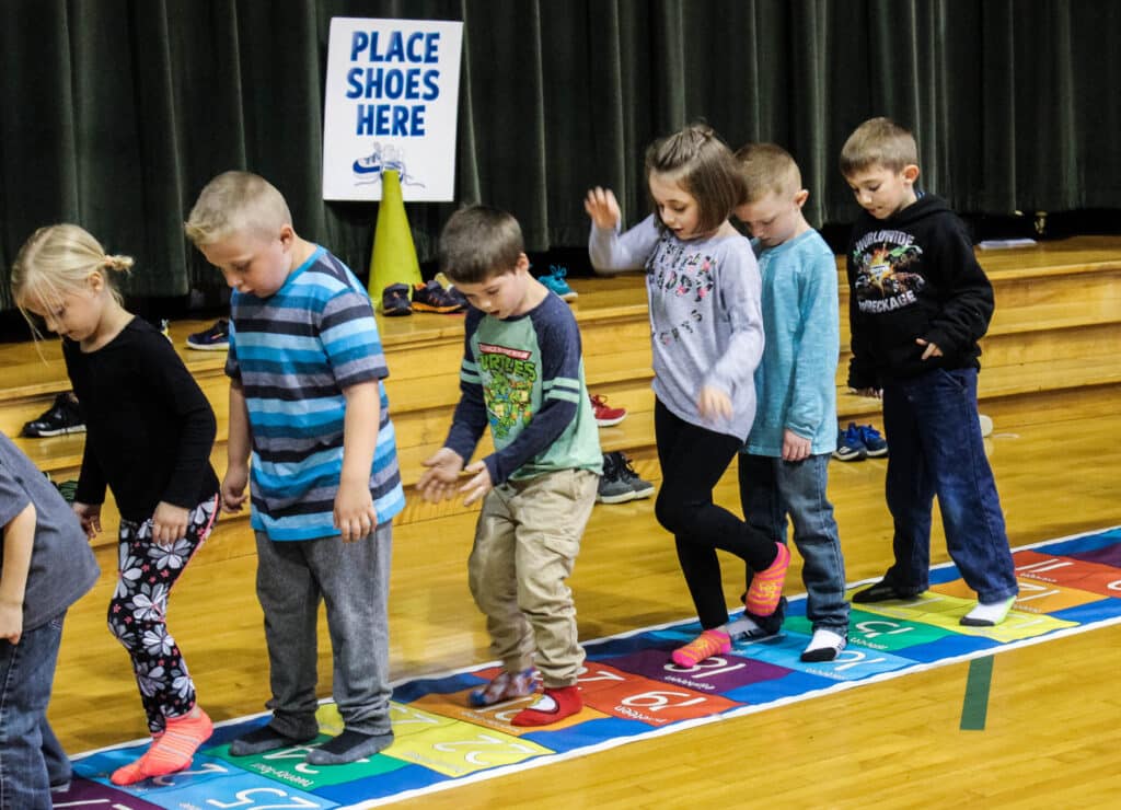 students on a hopscotch by 3s mat