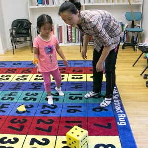 student and mother rolling a dice on add/subtract rug